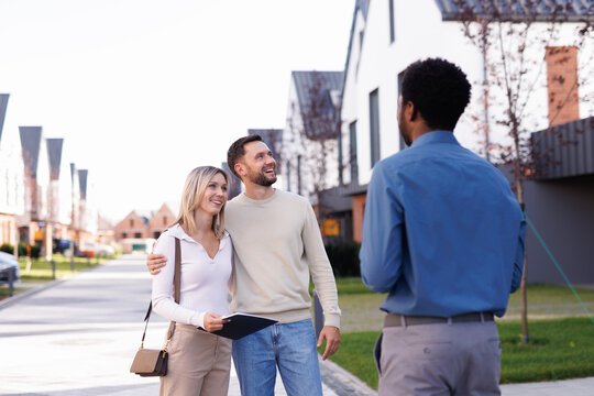 Black male realtor showing modern townhouse complex to couple hugging