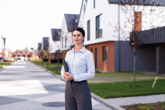 Portrait of female realtor with tablet in front of townhouse complex