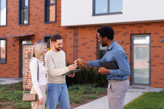 Woman looking at boyfriend taking key of house from black male realtor