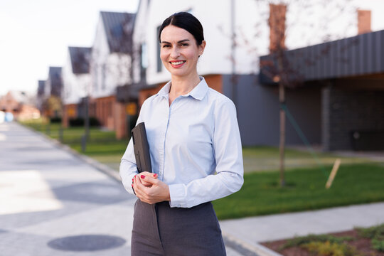Portrait of smiling adult female realtor at modern townhouse complex
