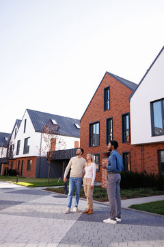 Realtor looking at couple hugging and looking at townhouse complex