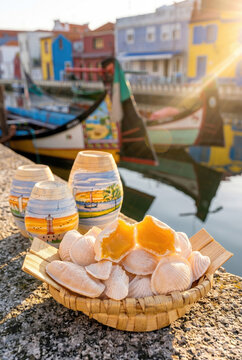 Traditional Portuguese ovos moles de Aveiro, shell-shaped sweets with moliceiro boats, colorful houses and the scenic ria de Aveiro in the background