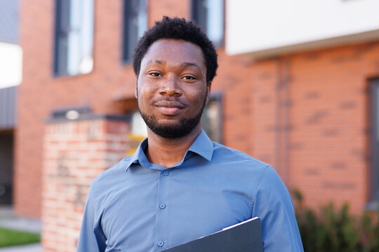 Portrait of smiling young black male realtor in front of townhouse