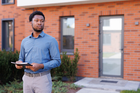 Concentrated black male realtor looking away in front of townhouse