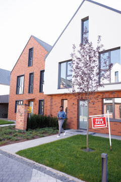 Black male realtor with copybook going on path in front of townhouse