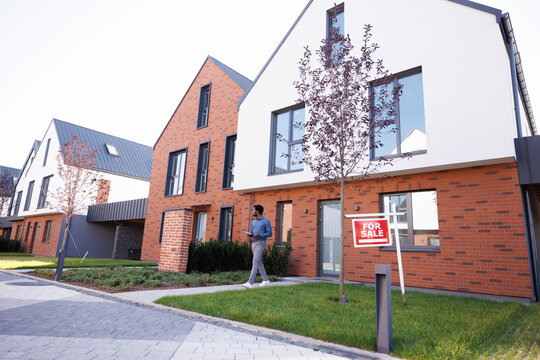 Young black male realtor with notebook going from modern townhouse