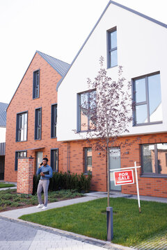 Thoughtful male realtor talking on smartphone on path near townhouse