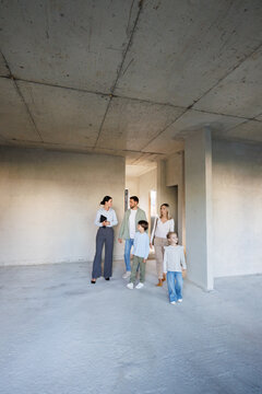 Adult female realtor showing new empty house inside to young family