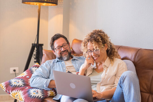 Middle-aged couple relaxing on couch at home, smiling while using a laptop together in a cozy living room