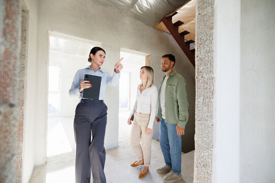 Realtor showing new empty house inside and pointing to young clients