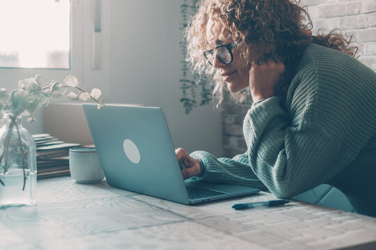 Woman working on laptop at home in cozy sweater and glasses, remote work and focused freelance setup