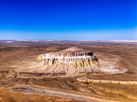 Aerial view of Airakty mountains with white limestone layers and eroded slopes under a clear blue sky Shetpe, Mangystau Region, Kazakhstan.