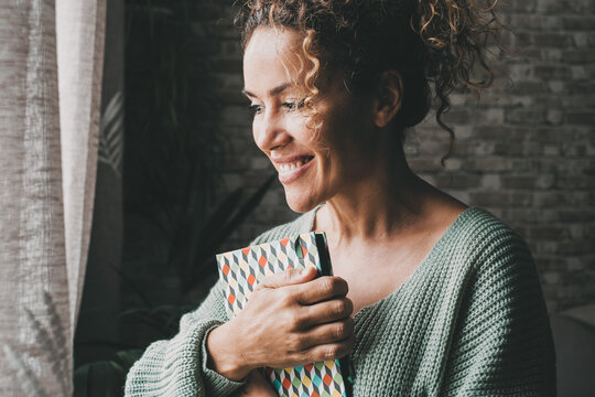 Smiling woman hugging a patterned journal at home, feeling grateful, cozy and reflective in sweater