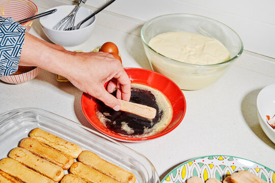 a man builds tiramisu layers with soaked ladyfingers