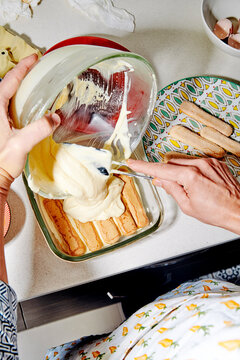 a man pours the final tiramisu cream over ladyfingers