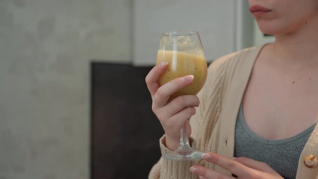 Pregnant caucasian woman inspecting smoothie glass, nutrition student hesitantly examining texture and aroma, careful hand on stem, close gaze evaluating safety and flavor, muted kitchen background,