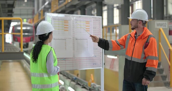 Rail engineers engaged in a planning and review session, focusing on a board displaying schedules, maintenance plans, and performance data of the rail systems. Ensuring efficient rail operations.