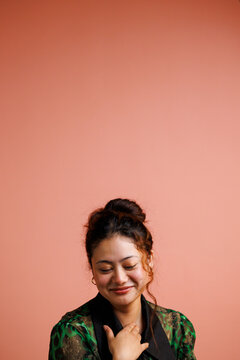 Woman Smiles With Hands Crossed in Front of Her on a Pink Wall