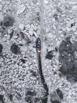 Tugboat creating black trail through dense white ice
