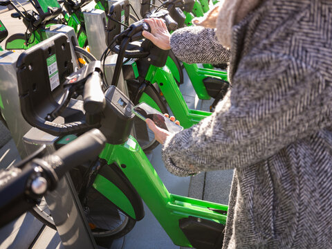 Woman unlocking green rental bike with smartphone