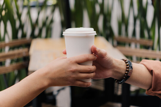 Hands passing a white coffee cup at an outdoor cafe