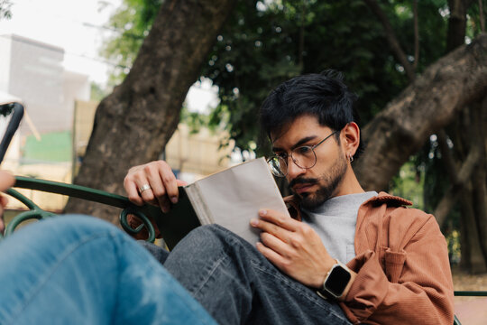 Focused young man reading a book on a bench in a sunny park