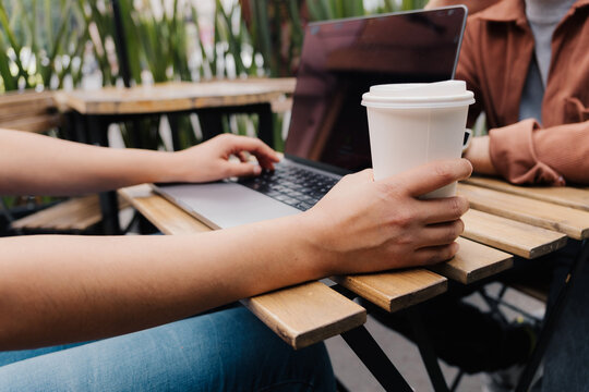 Close up of hands using laptop and holding coffee at a cafe