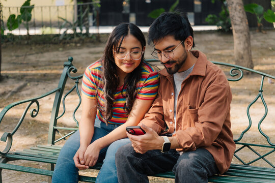 Young couple sitting on a park bench looking at a smartphone