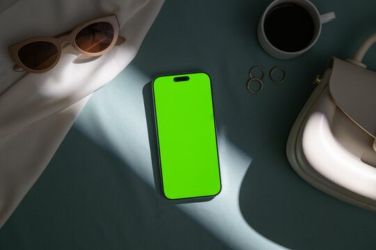 Flat lay of a smartphone with green screen, sunglasses, coffee and bag