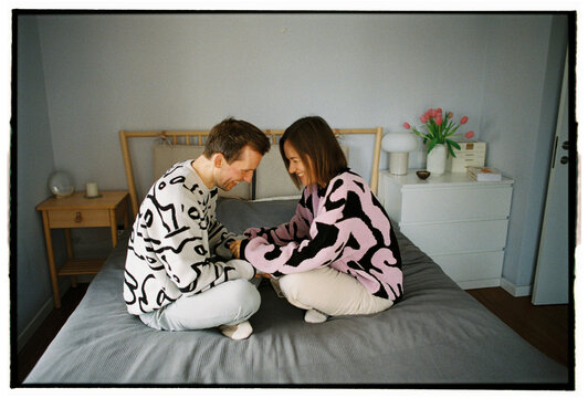 Couple laughing and holding hands sitting on bed at home