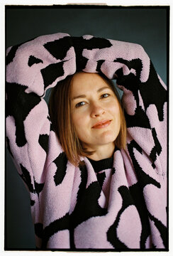 Woman in cozy sweater with arms raised looking at camera