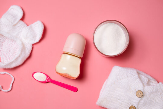Baby bottle with milk powder and knitted hat on pink background