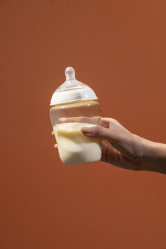Hand holding a baby bottle filled with milk against a warm backdrop