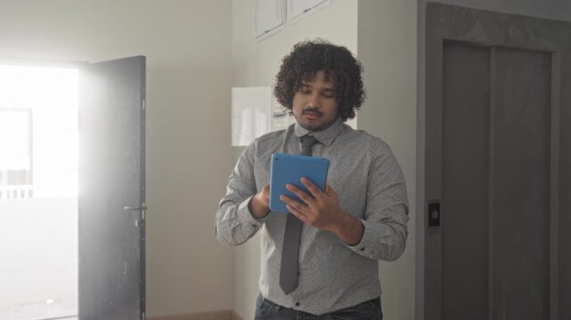 Man holding blue tablet tapping screen with hands in a building doorway wearing shirt and tie; confidence property sales.