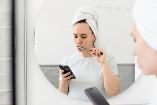 Woman Brushing Teeth While Using Smartphone in Bathroom