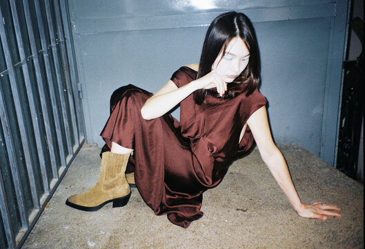 Woman in Brown Dress Sits in Urban Space at Night
