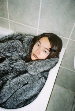 Person Sits in Bathtub Wrapped in Fur in Indoor Setting