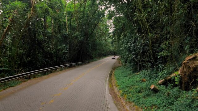 Aerial view of winding highway through Atlantic Forest with car driving on Rodovia Cunha-Paraty. Push in and follow camera movement