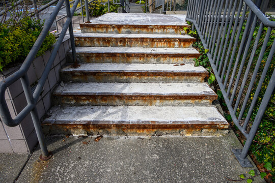 Looking up old outdoor staircase with tiles removed showing mastic adhesive and rusty iron lip, black metal railings
