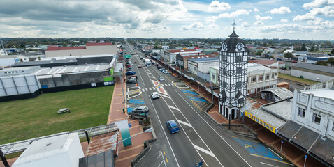 Fototapeta premium A view of the clock tower and street in Statford, Taranaki, New Zealand. Cars drive along the road and park in designated spots.