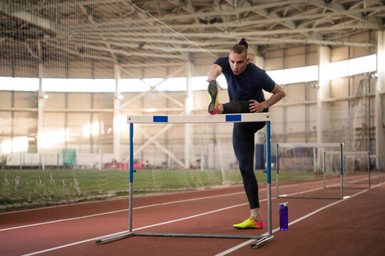 Young male athlete stretching near barrier