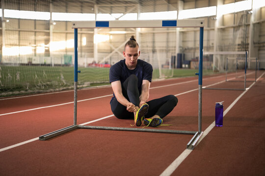 Young sportsman tying shoelaces near hurdle