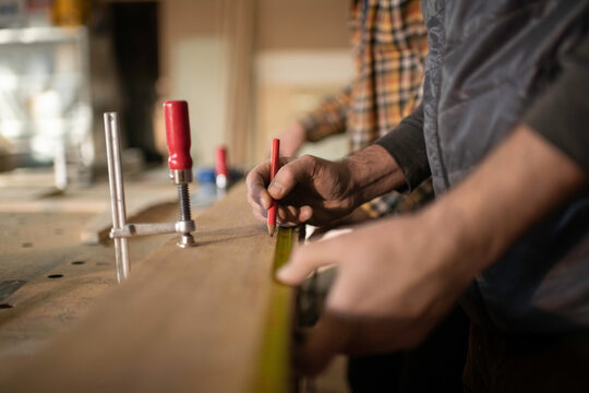 Cropped craftsman making marks on wood near colleague