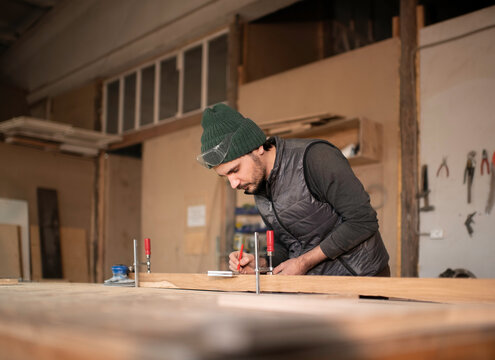 Male carpenter making marks on plank