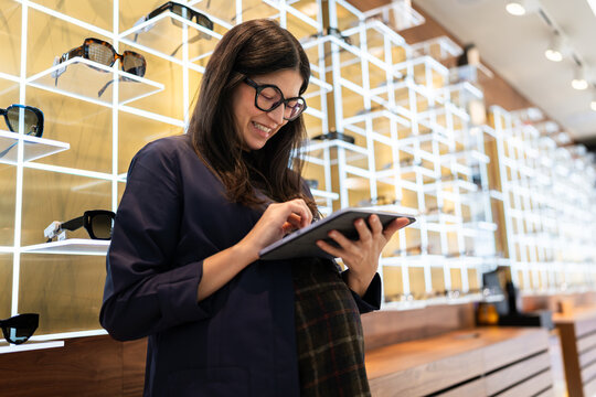 Pregnant optometrist working in eyewear store using tablet