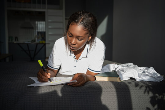 Black student doing homework on bed