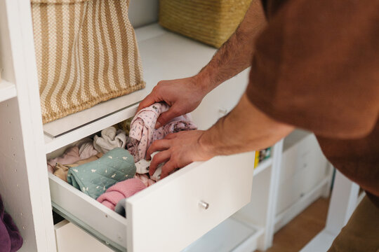 Parent organizing baby clothes in nursery drawer at home