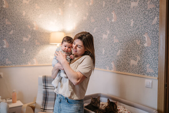 Parent holding infant in nursery with pet cats