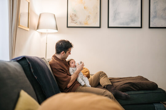 Parent bottle feeding baby on sofa at home