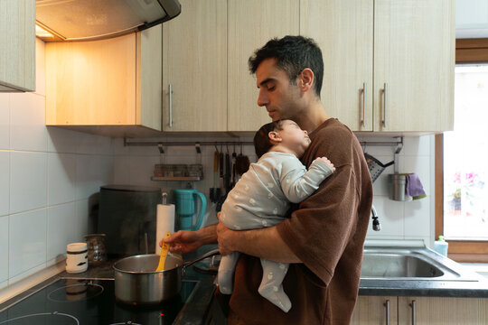 Parent cooking while holding sleeping baby at home